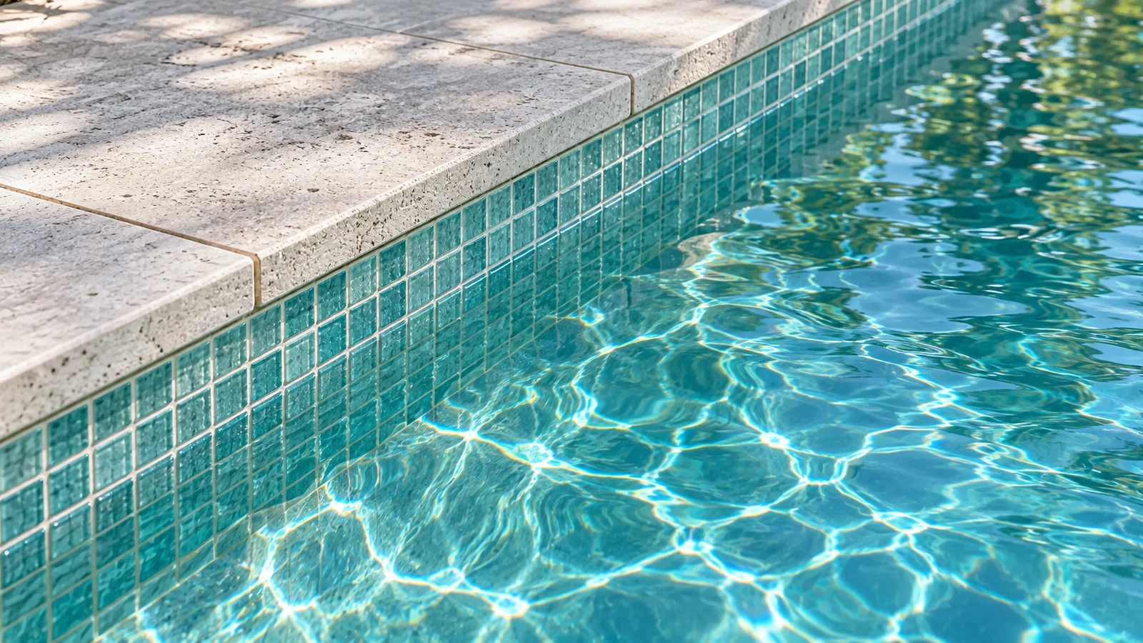 Close view of pale stone coping meeting aqua waterline mosaic
